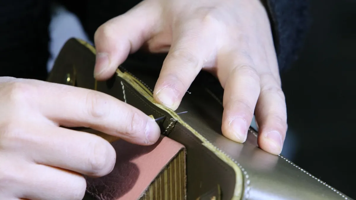 Hands checking the stitching on a leather bag sample